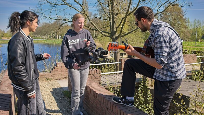 Drie jongeren die met een camera een guitaar spelende jongere filmt