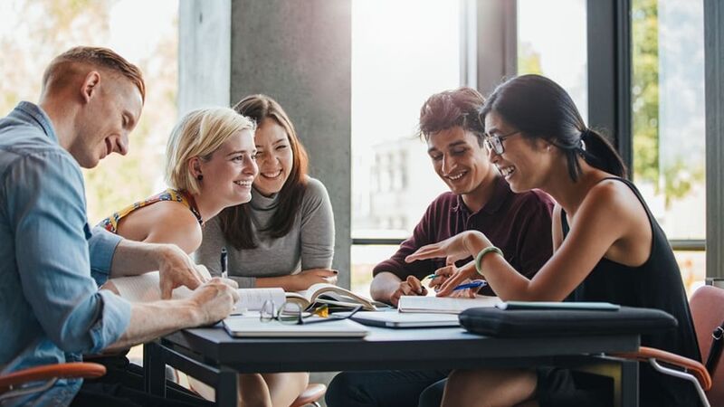 Groep lachende jonge mensen aan tafel met schriften en boeken op tafel