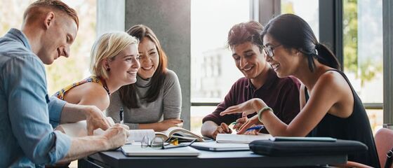 Groep lachende jonge mensen aan tafel met schriften en boeken op tafel